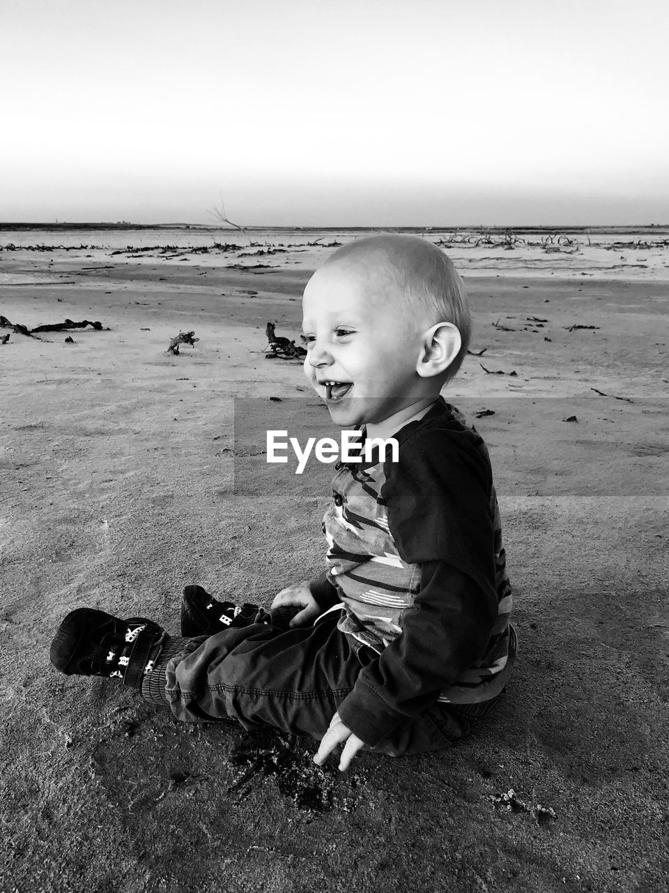 Side view of happy baby boy sitting at beach