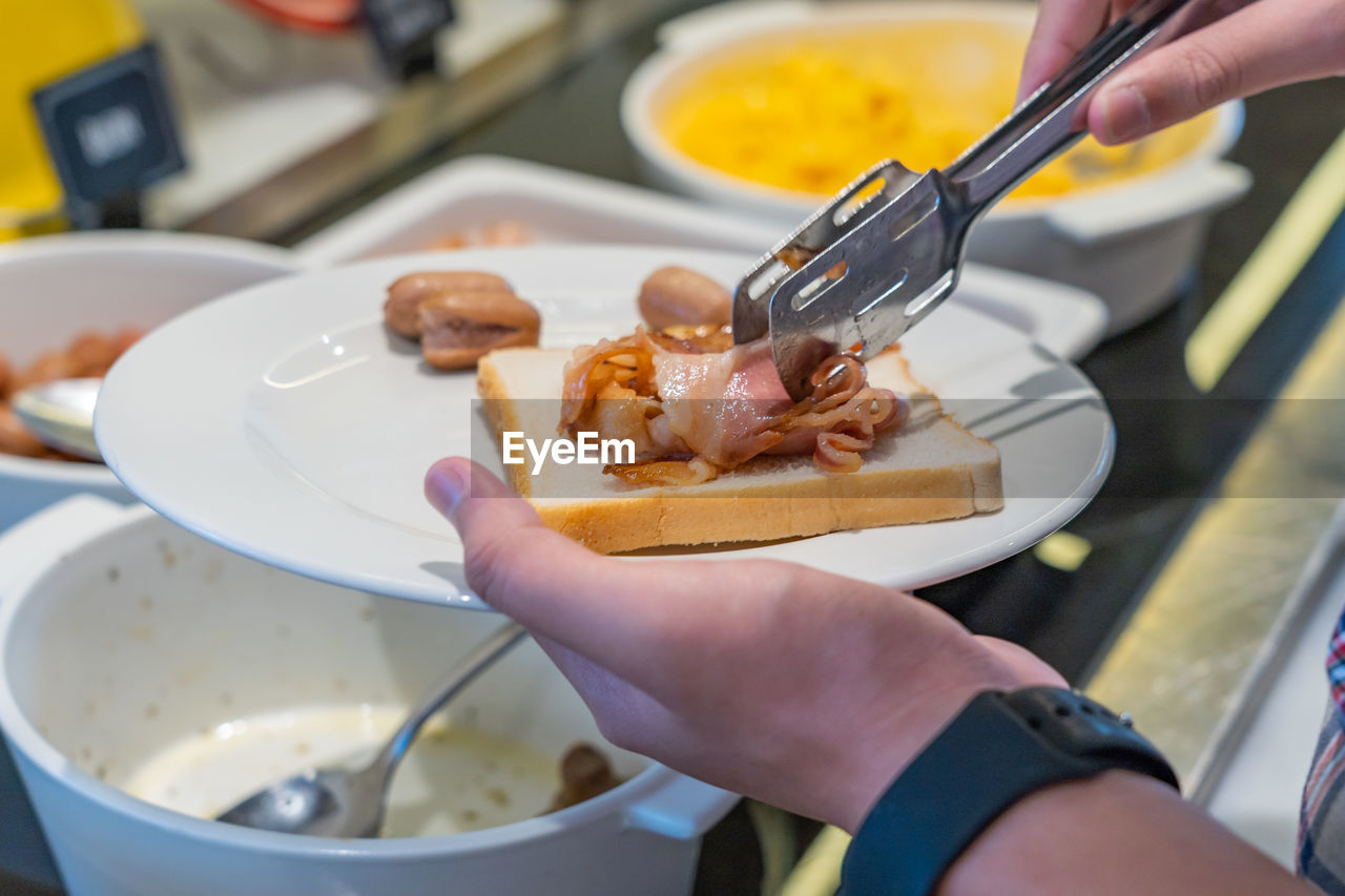 Closeup photo of human picking bacon and sandwich at buffet