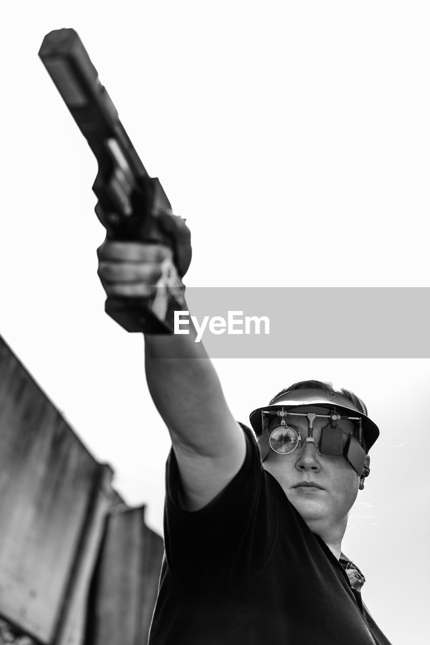 LOW ANGLE VIEW OF YOUNG MAN HOLDING CAMERA AT HOME