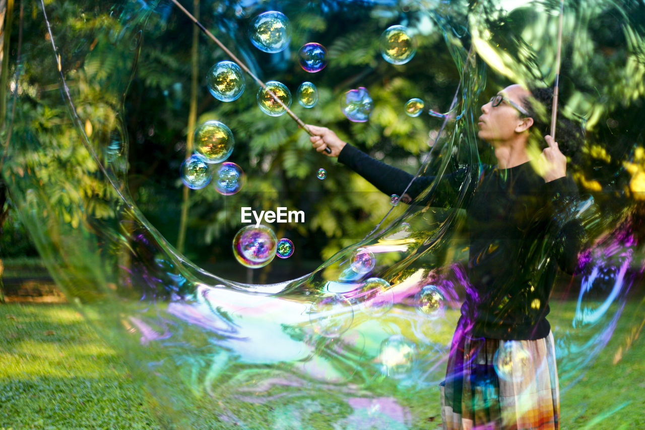 Street artist making rainbow bubbles at park 