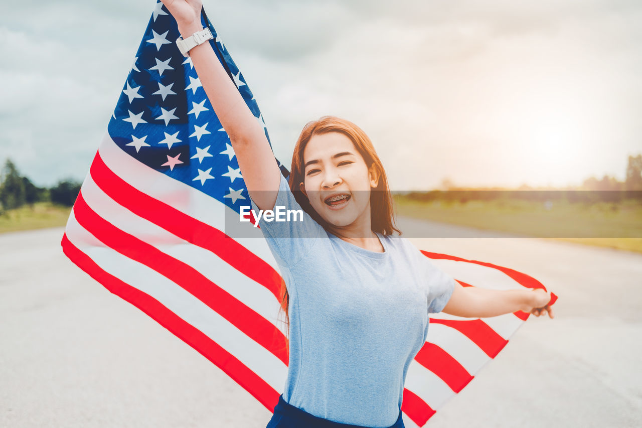 Portrait of smiling teenage girl with american flag standing on road