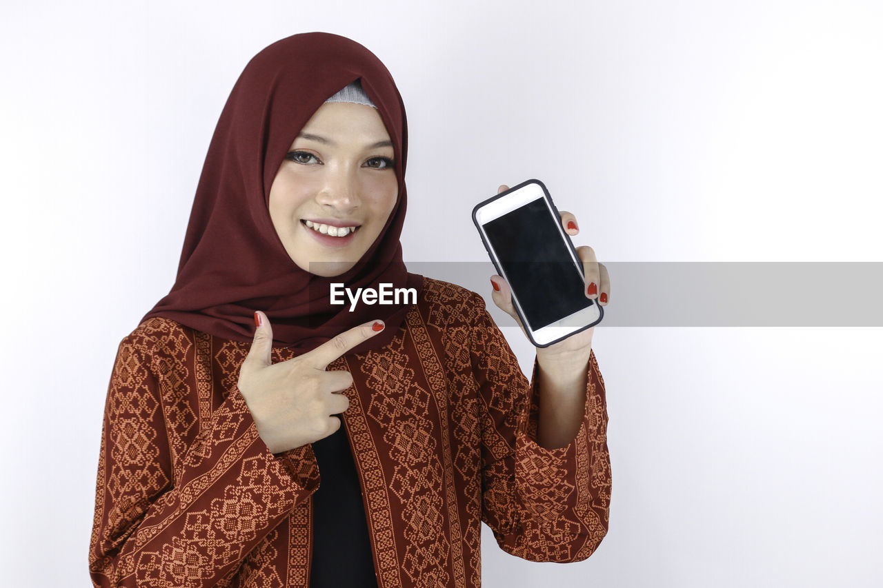 PORTRAIT OF SMILING YOUNG WOMAN USING MOBILE PHONE