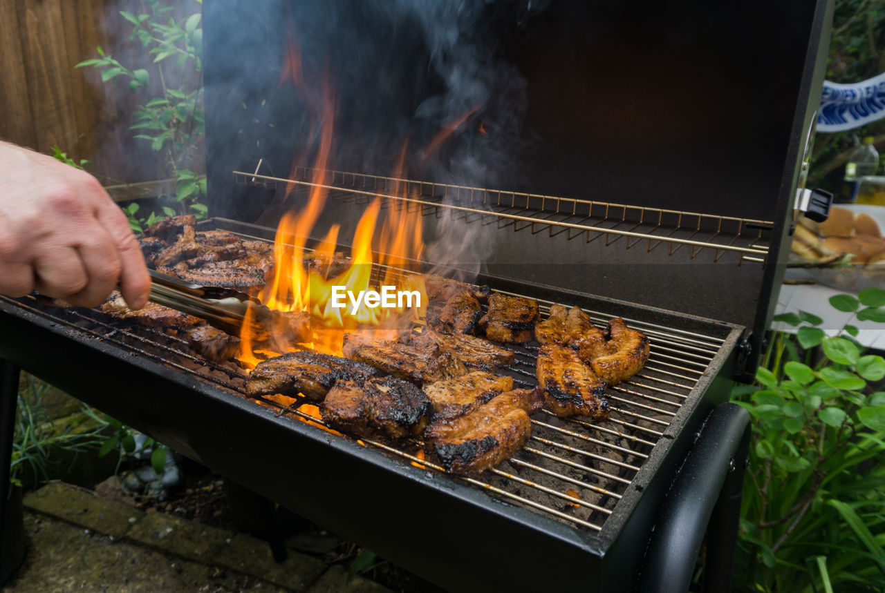 Cropped hand preparing meat on barbecue grill