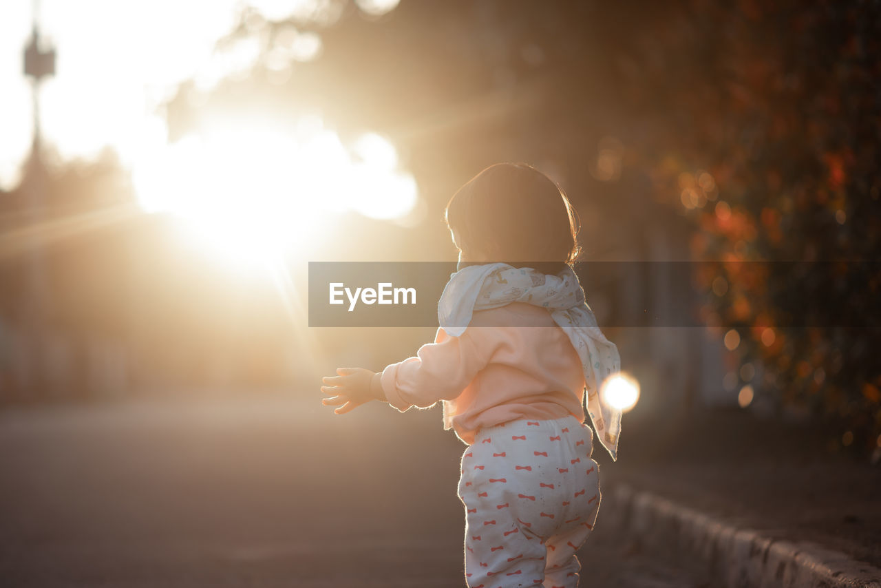 Rear view of girl standing on land during sunset