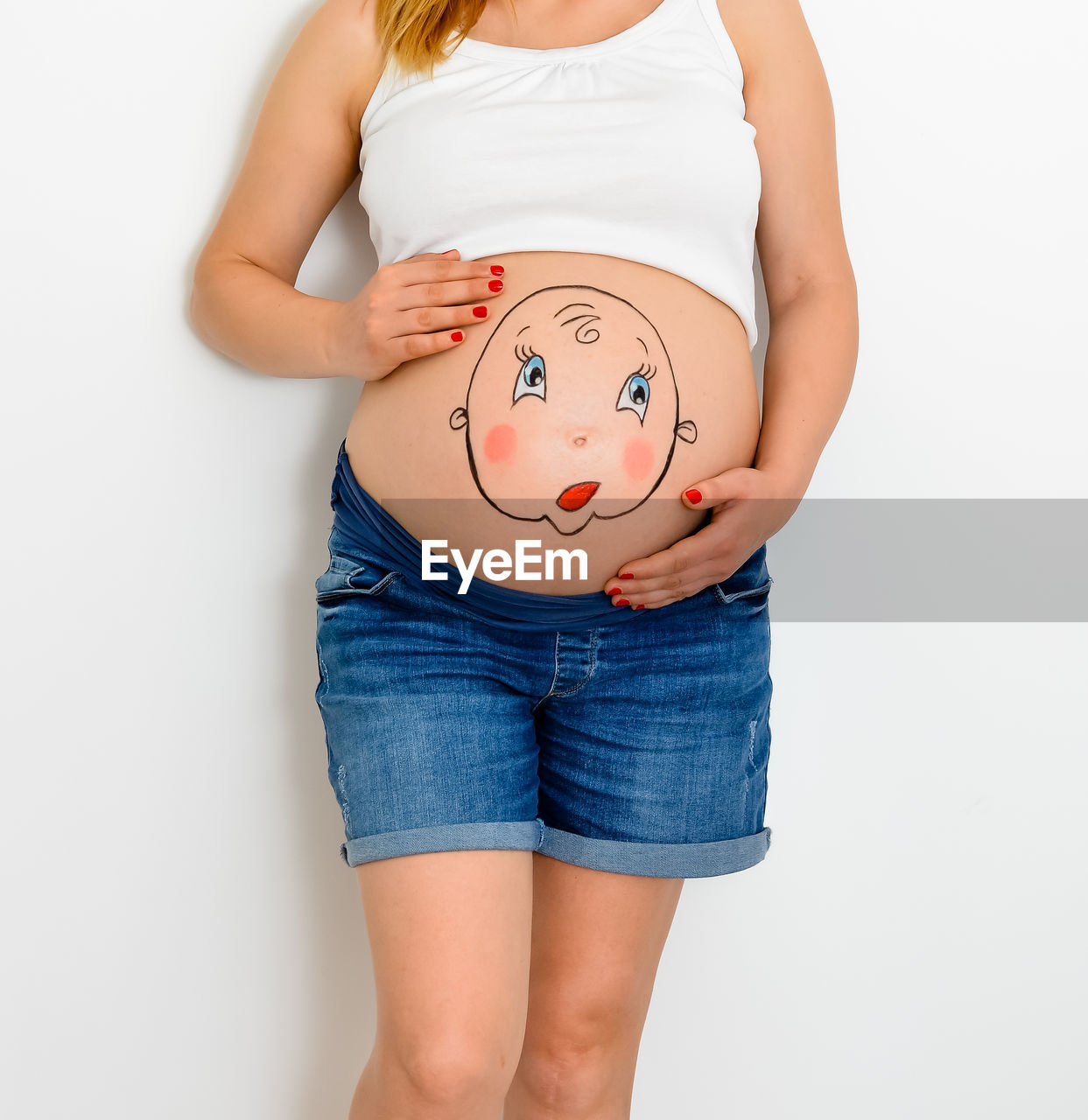 Midsection of pregnant woman with painting belly standing against white background