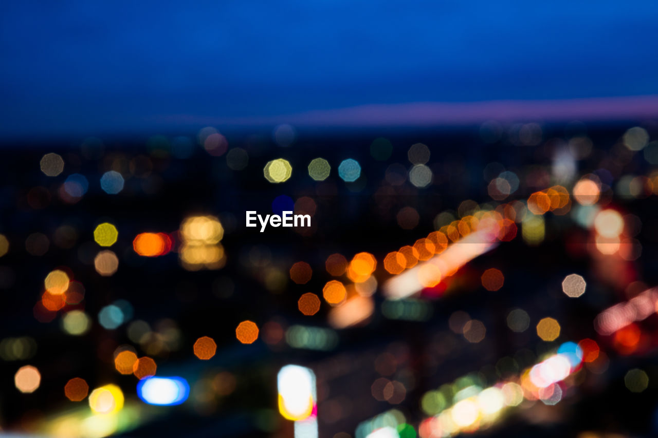 Defocused image of illuminated city against sky at night