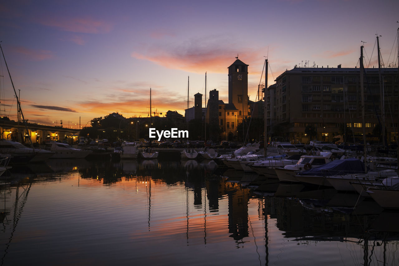 SAILBOATS MOORED IN HARBOR AGAINST BUILDINGS IN CITY