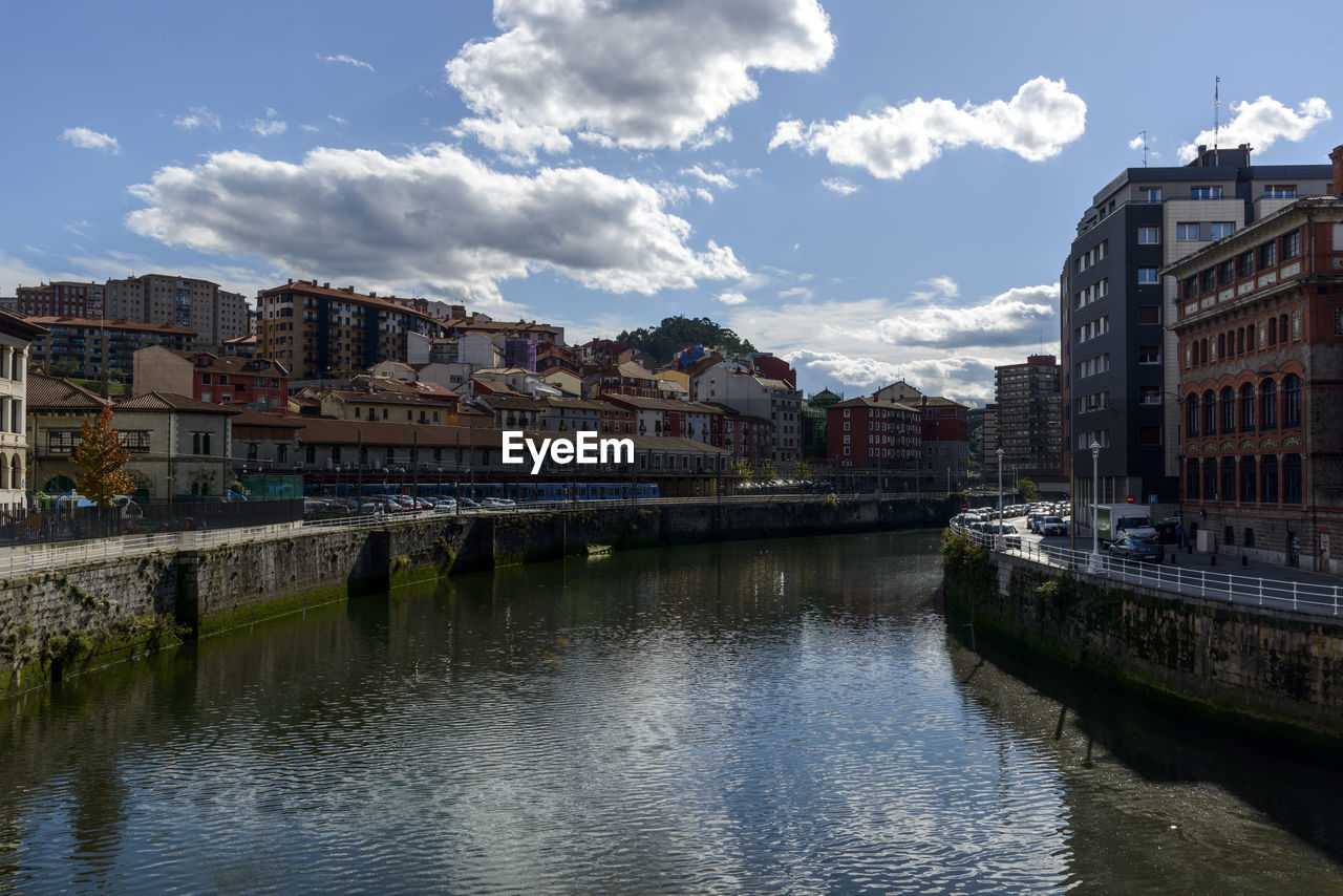 BUILDINGS BY RIVER AGAINST SKY IN CITY