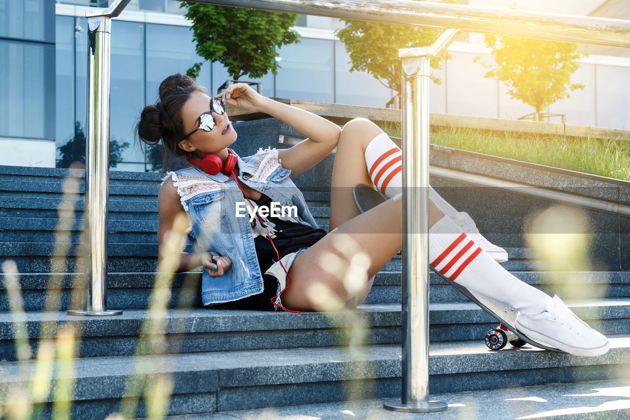 full length of young woman sitting on metal gate