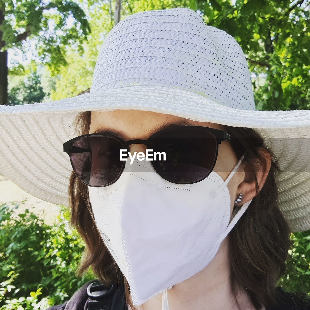 Portrait of woman wearing hat, sunglasses and face mask ffp2 / kn95 on a sunny day outdoors 
