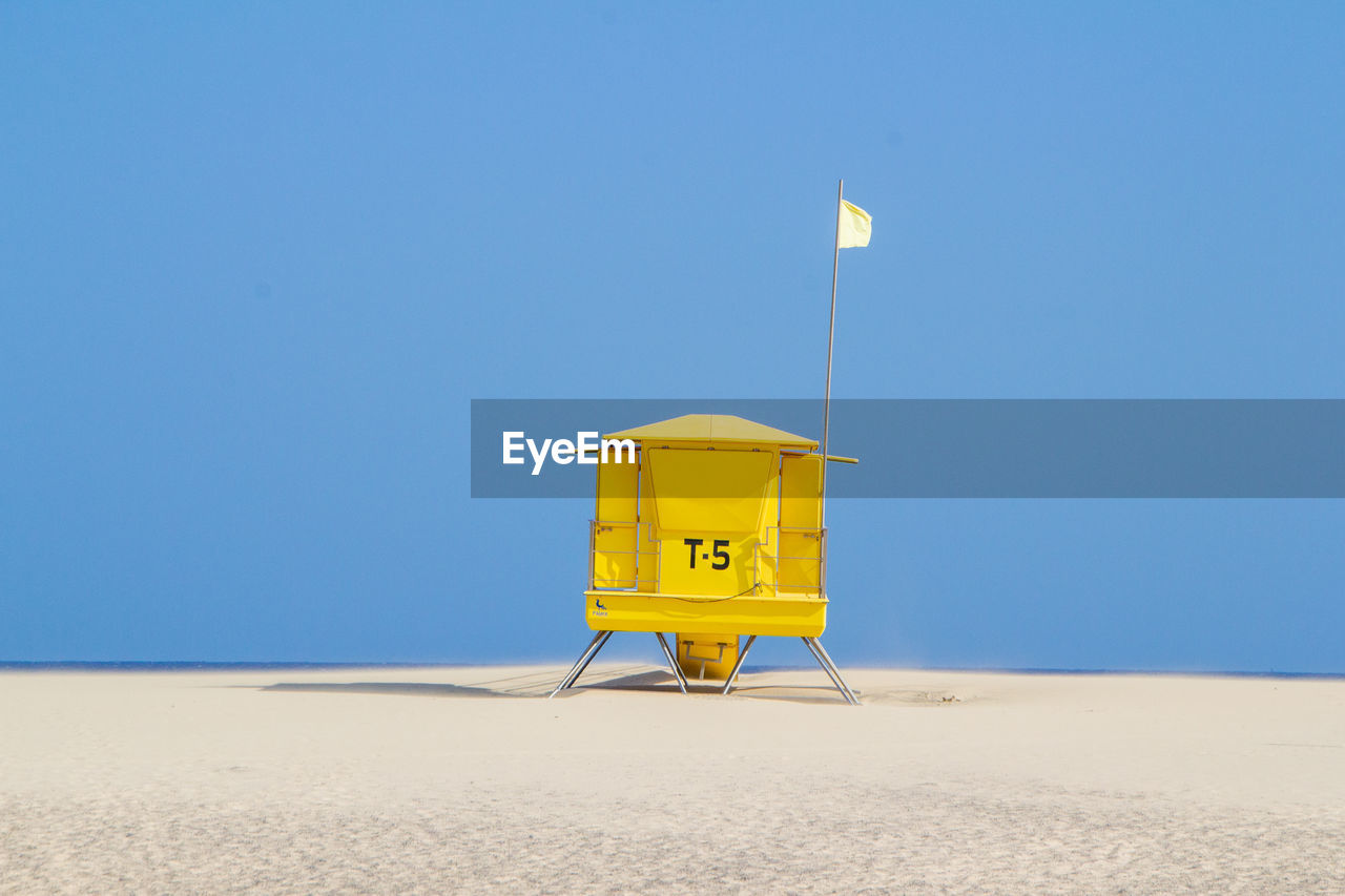 Lifeguard hut on beach against clear blue sky with flag raised seems a lander