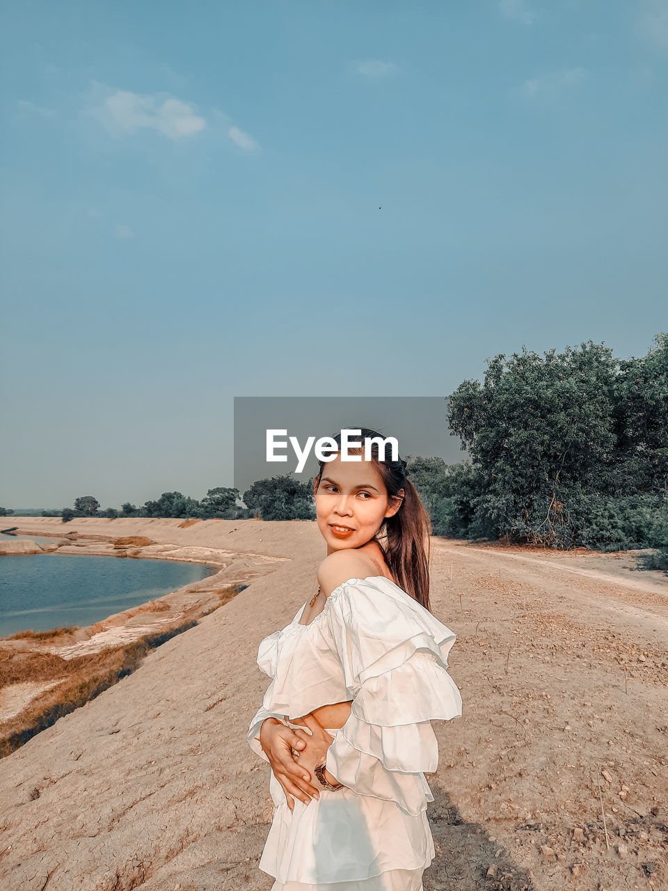 Portrait of smiling young woman standing on land against sky