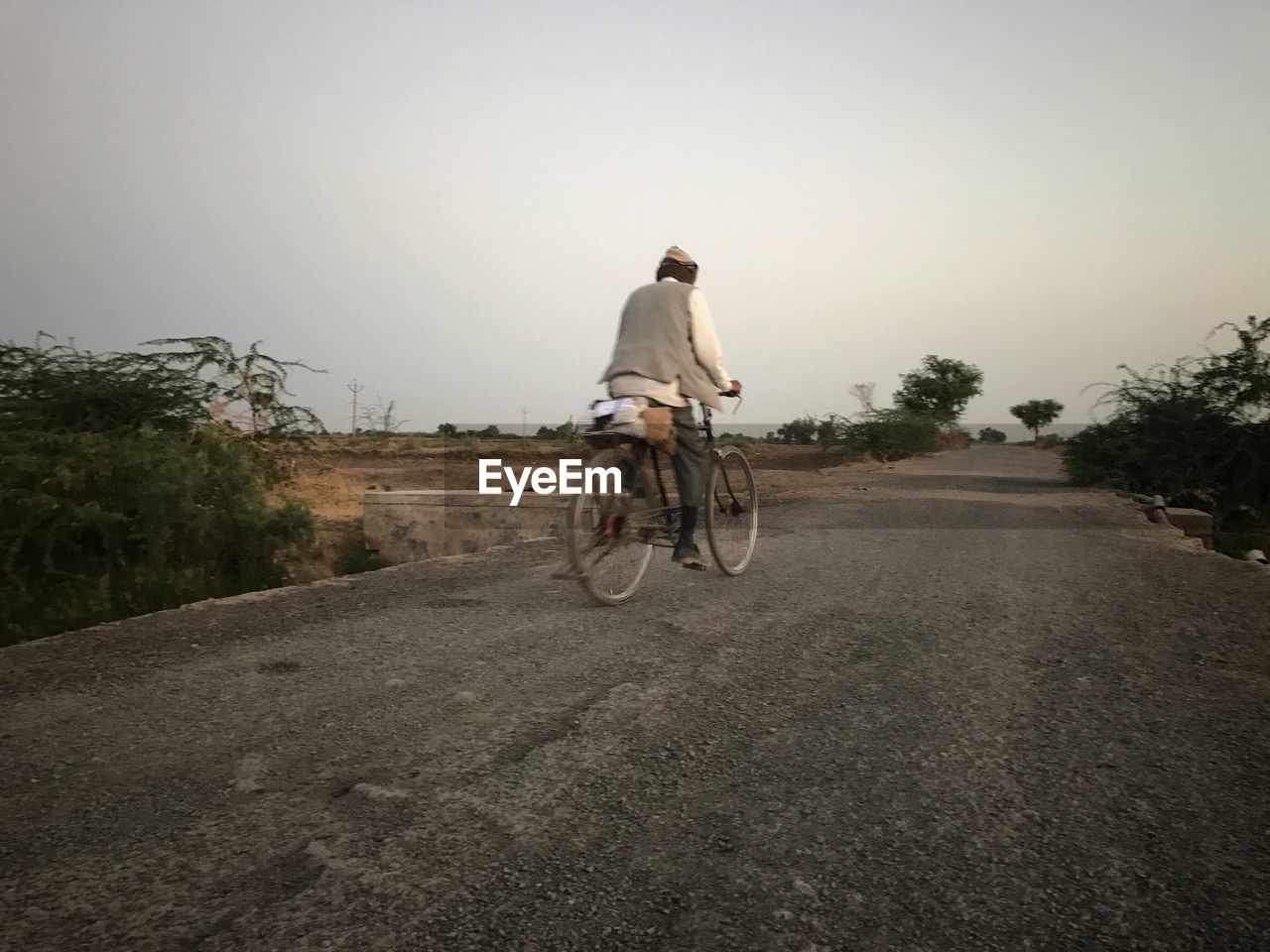 MAN RIDING BICYCLE ON ROAD AGAINST TREES