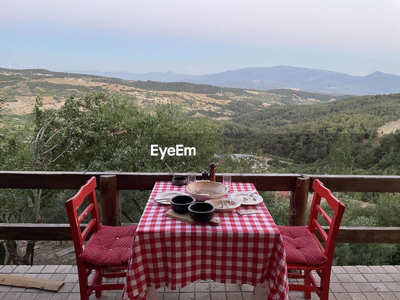 table, seat, mountain, chair, nature, scenics - nature, no people, food and drink, landscape, beauty in nature, plant, tranquility, mountain range, sky, absence, tranquil scene, tablecloth, tree, furniture, idyllic, land, outdoors, relaxation, day, travel destinations, food, balcony, drink, architecture, summer, wood, environment, setting, empty, non-urban scene, holiday, red, vacation, travel, checked pattern, trip, railing, clear sky, patio