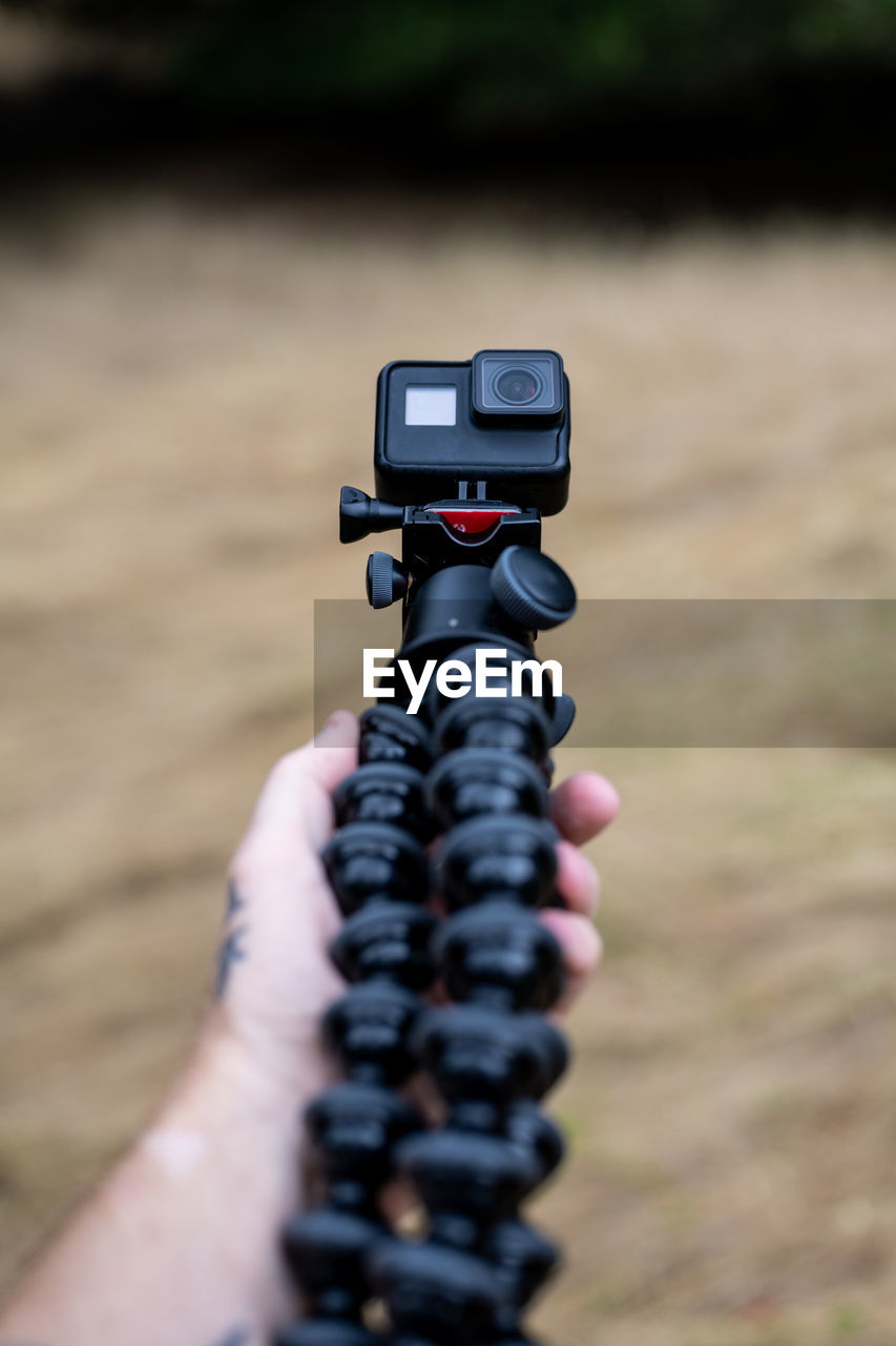 Hand holding tripod with action camera over brown grass in field