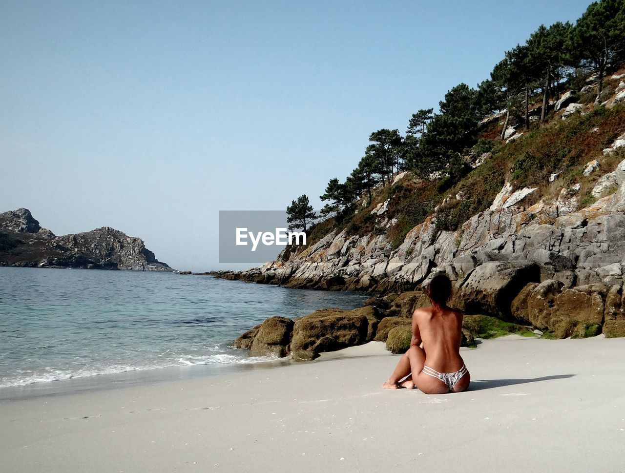 Rear view of topless woman sitting at beach