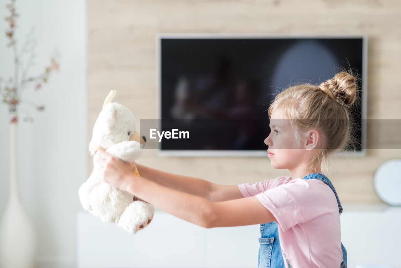 Side view of girl playing with teddy bear at home