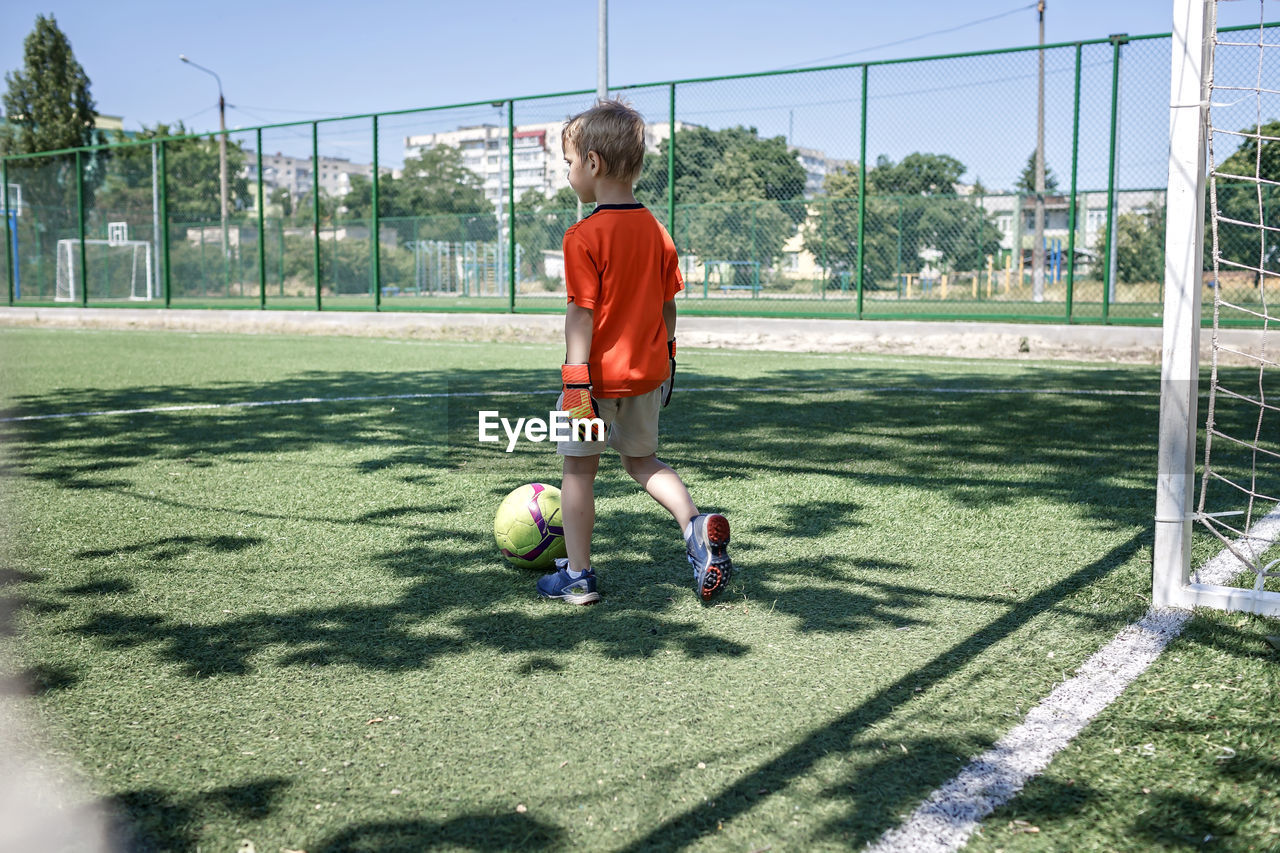 Little boy in black and orange form playing football on field, young soccer player, goalkeeper