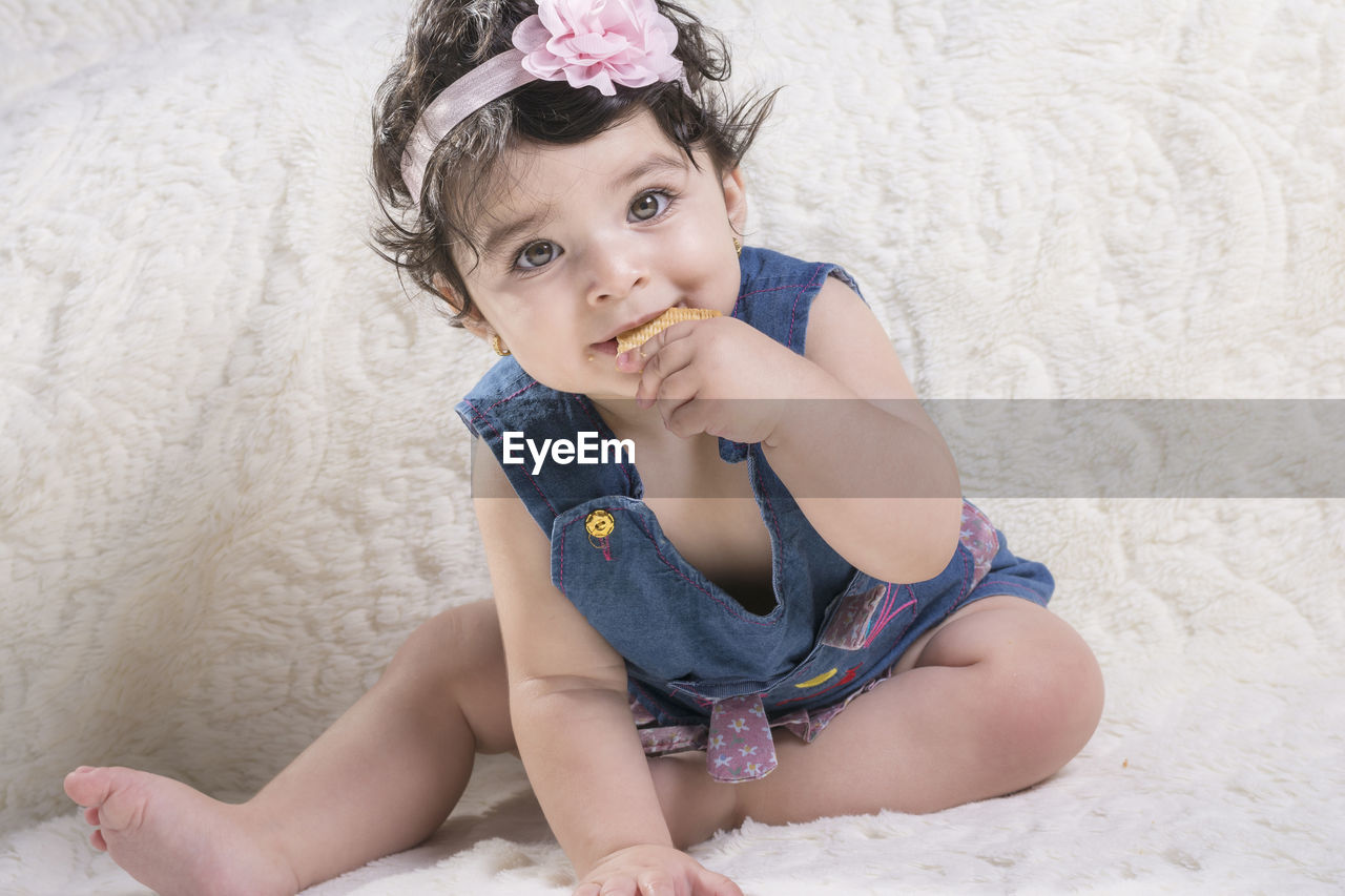 Portrait of cute girl eating biscuit while sitting on bed at home