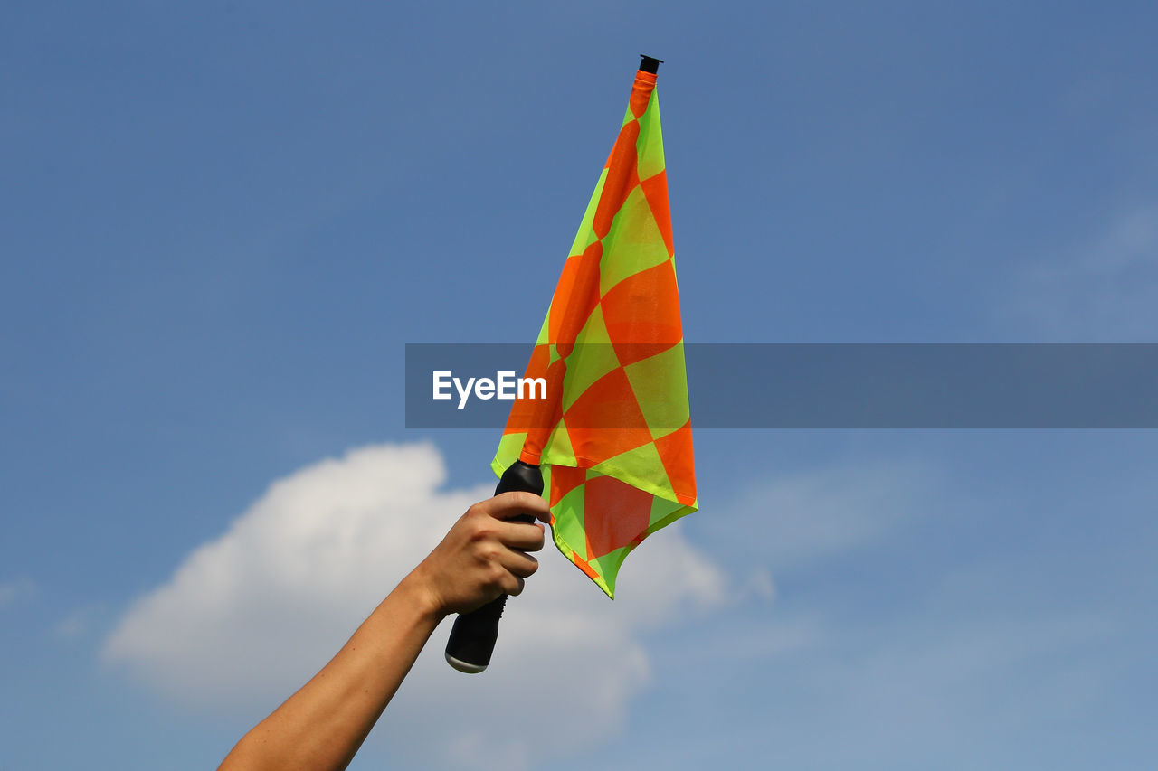Low angle view of hand holding flag against blue sky