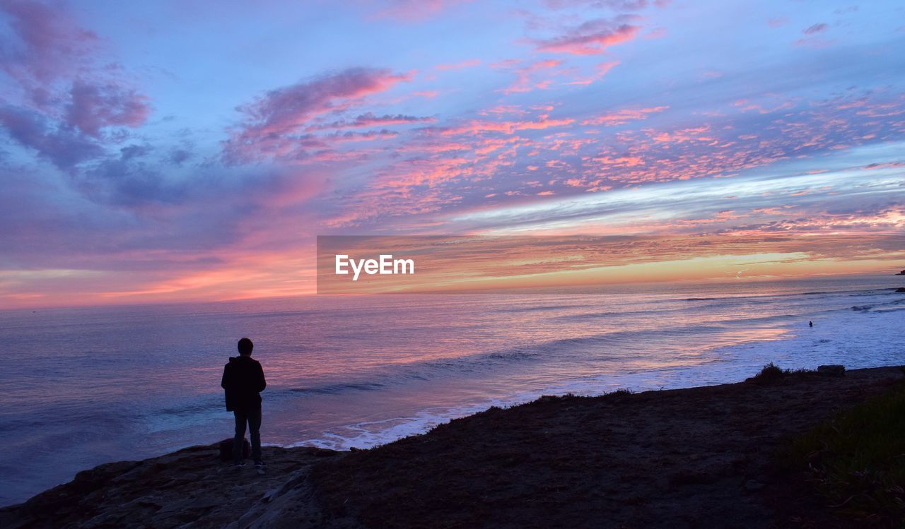 Silhouette man standing on shore against sky during sunset