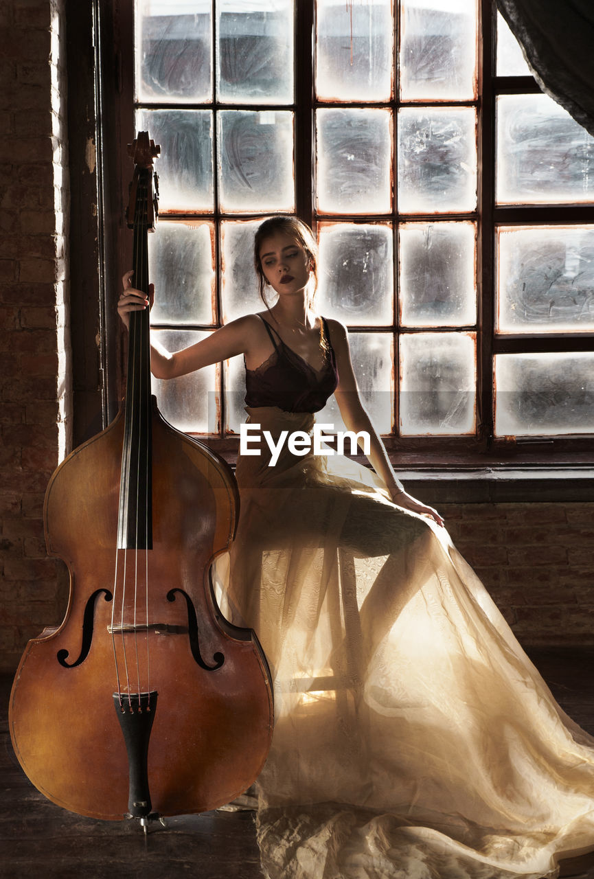 Young woman with double bass sitting on stool at home