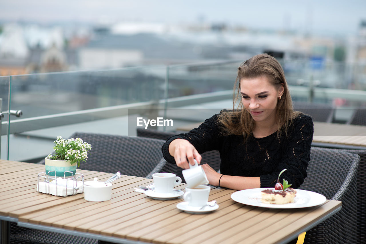 Young smiling woman female having breakfast on the hotel 's restaurant outdoor terrace