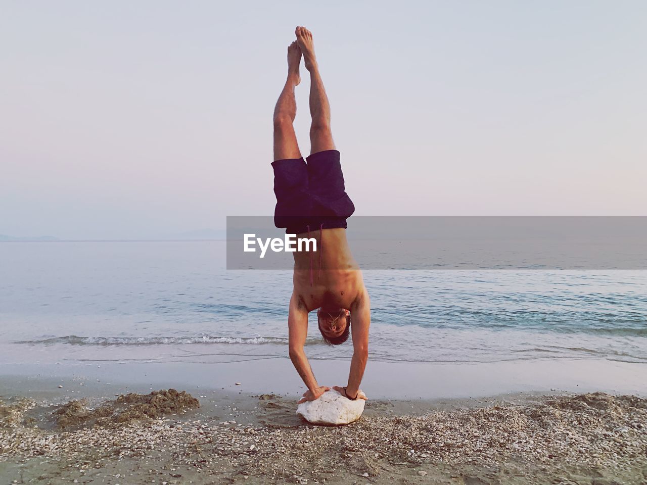 Full length of shirtless man doing handstand at beach against sky