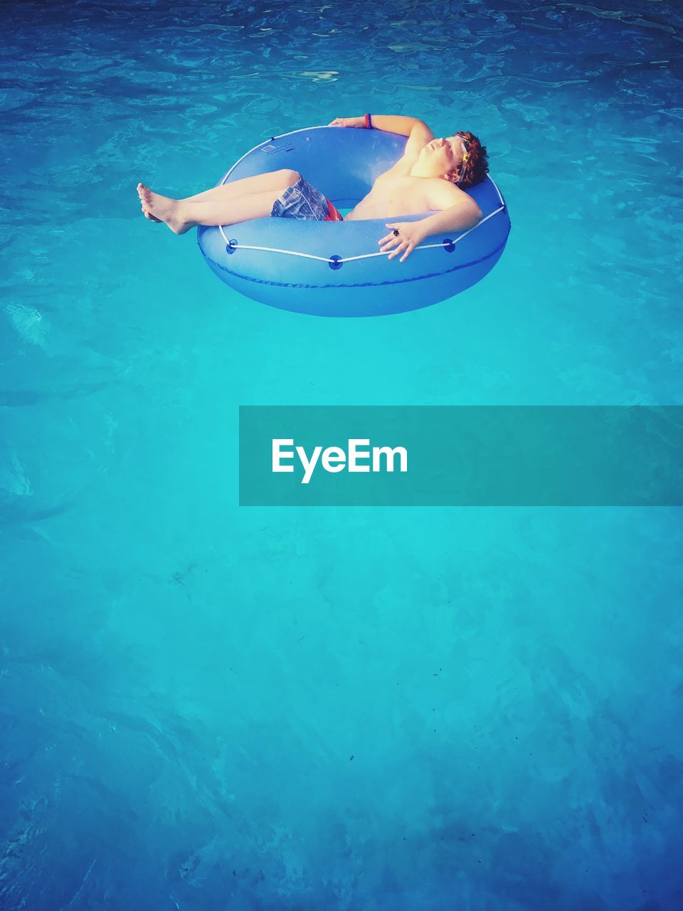 Shirtless boy relaxing in inflatable ring at swimming pool