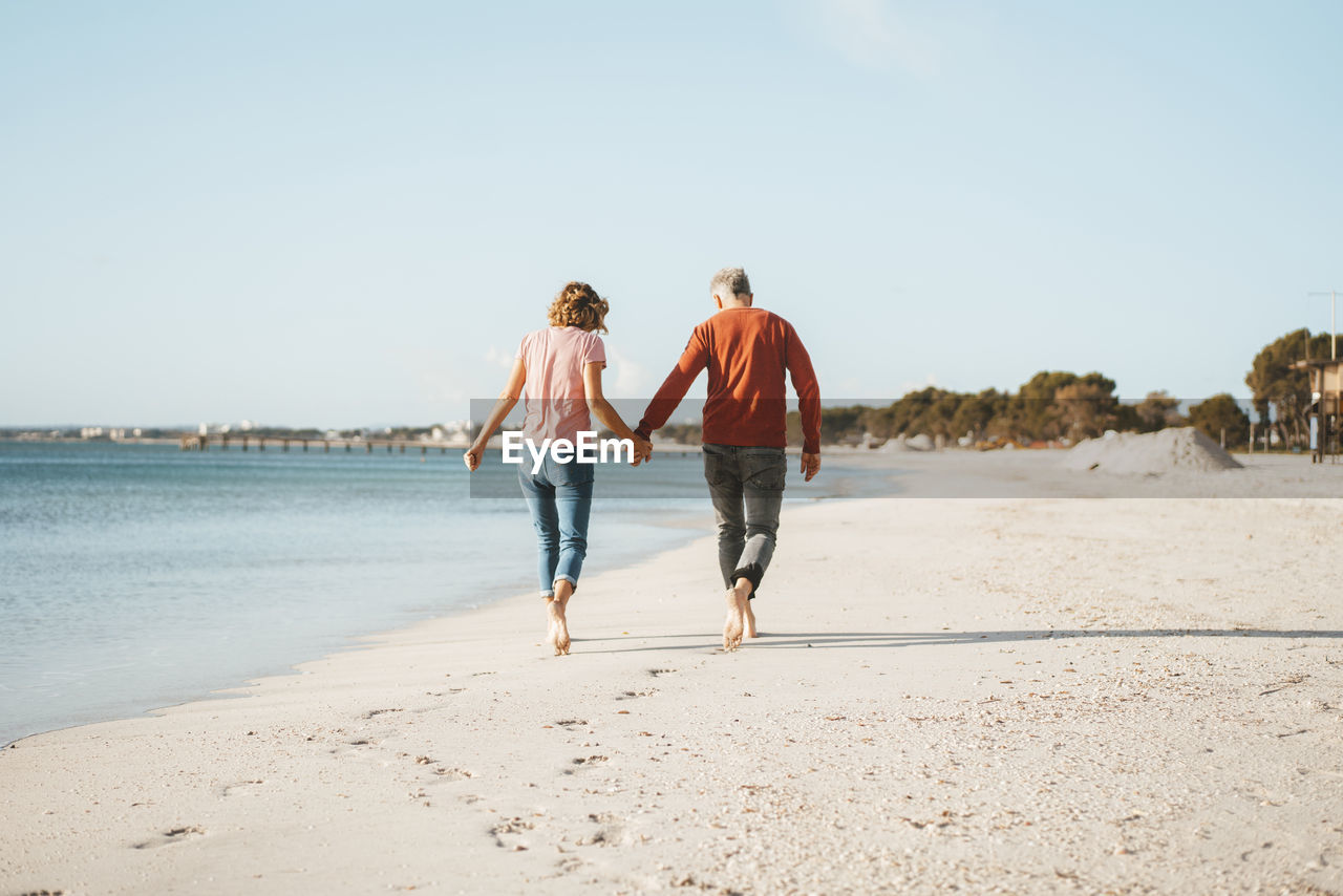 Couple holding hands walking on shore at beach