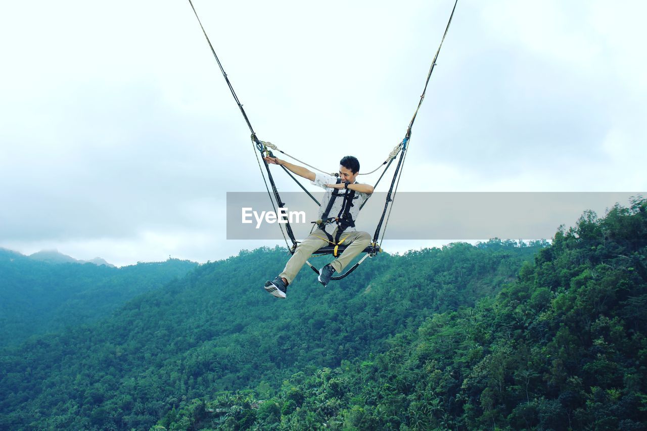 Low angle view of man hanging on rope against sky