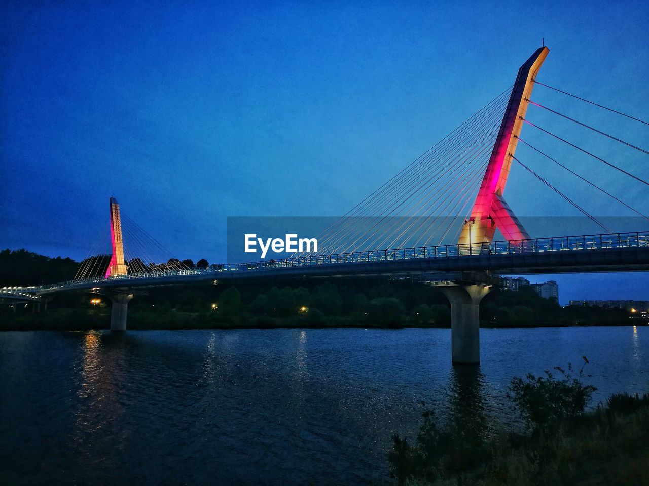 Low angle view of suspension bridge over river against blue sky