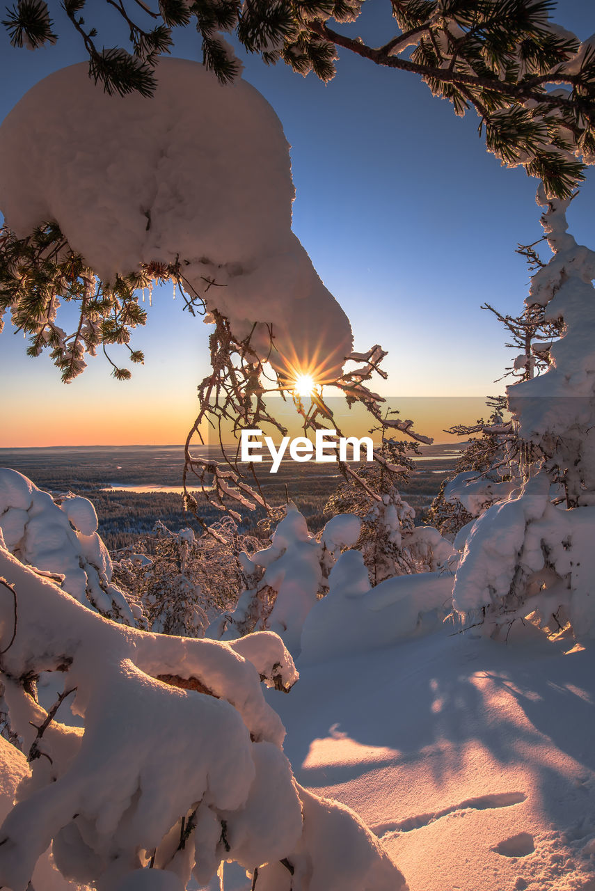 Snow covered land against sky during sunset