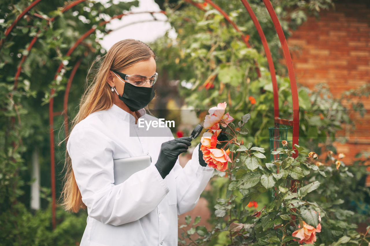 YOUNG WOMAN STANDING BY FLOWERING PLANTS