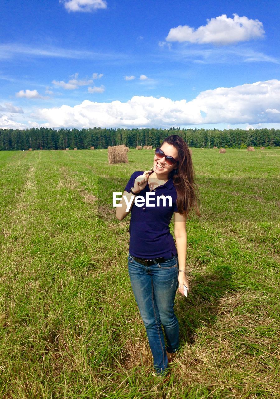 Portrait of young woman standing on farm field against blue sky