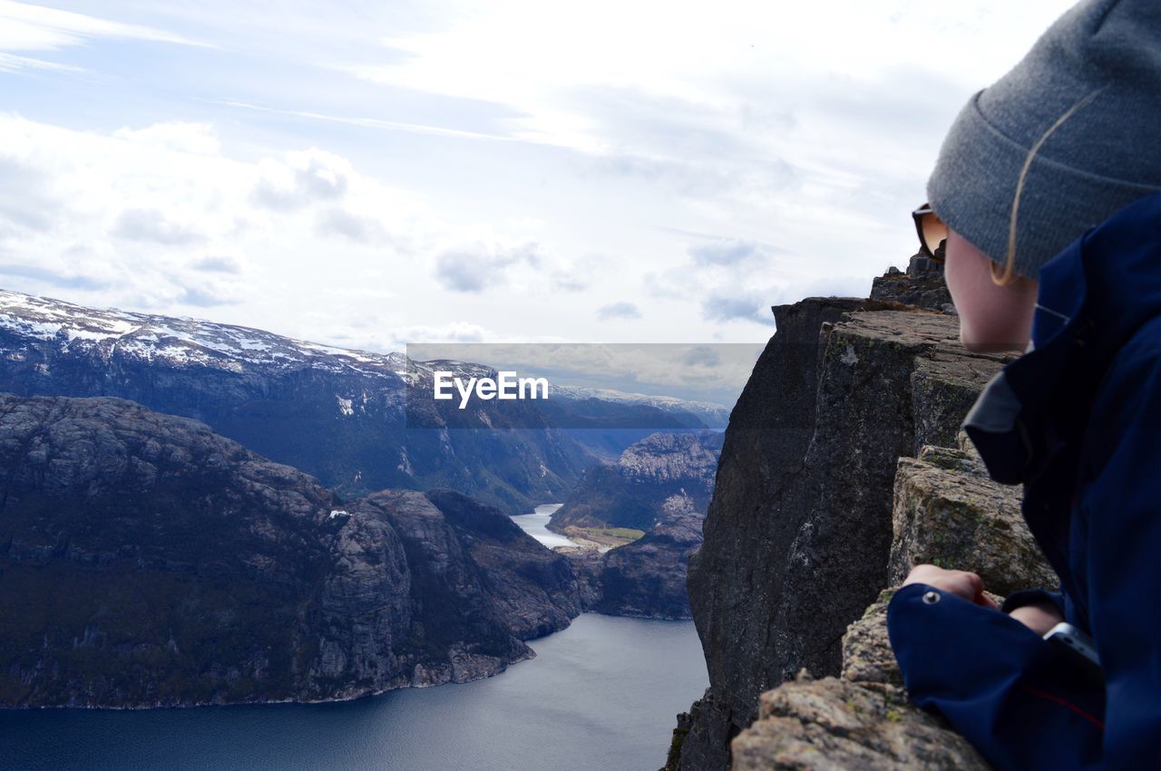 Woman leaning on retaining wall while looking at mountains against sky