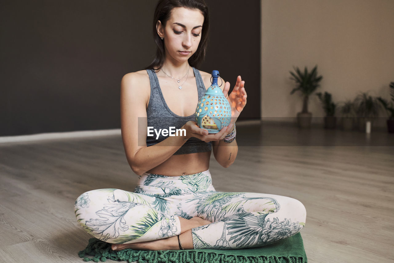 Young woman meditates alone in yoga studio with aroma lamp