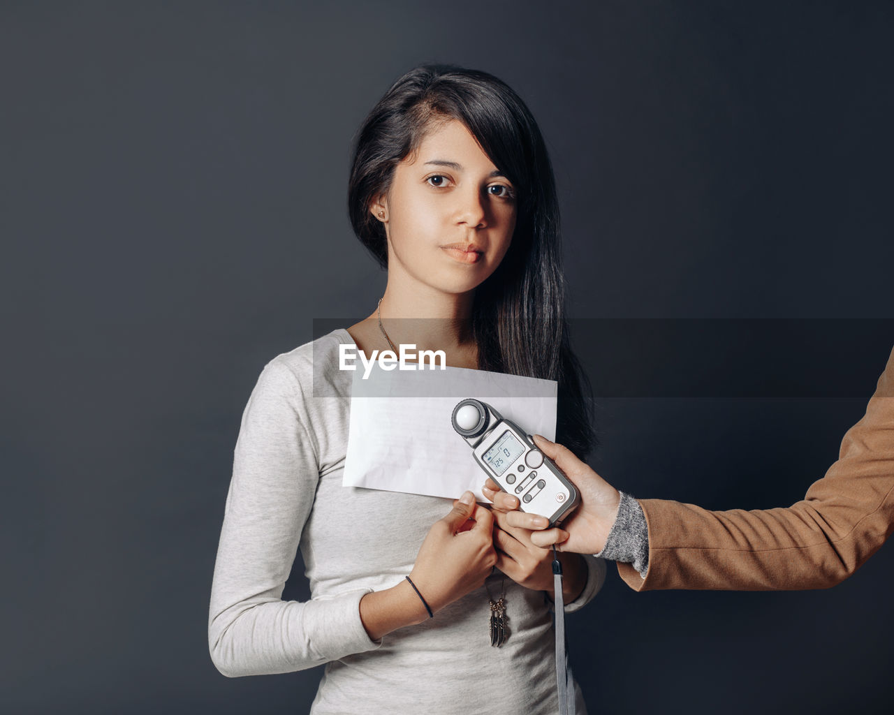 Cropped hand of person holding light meter over woman standing against gray background