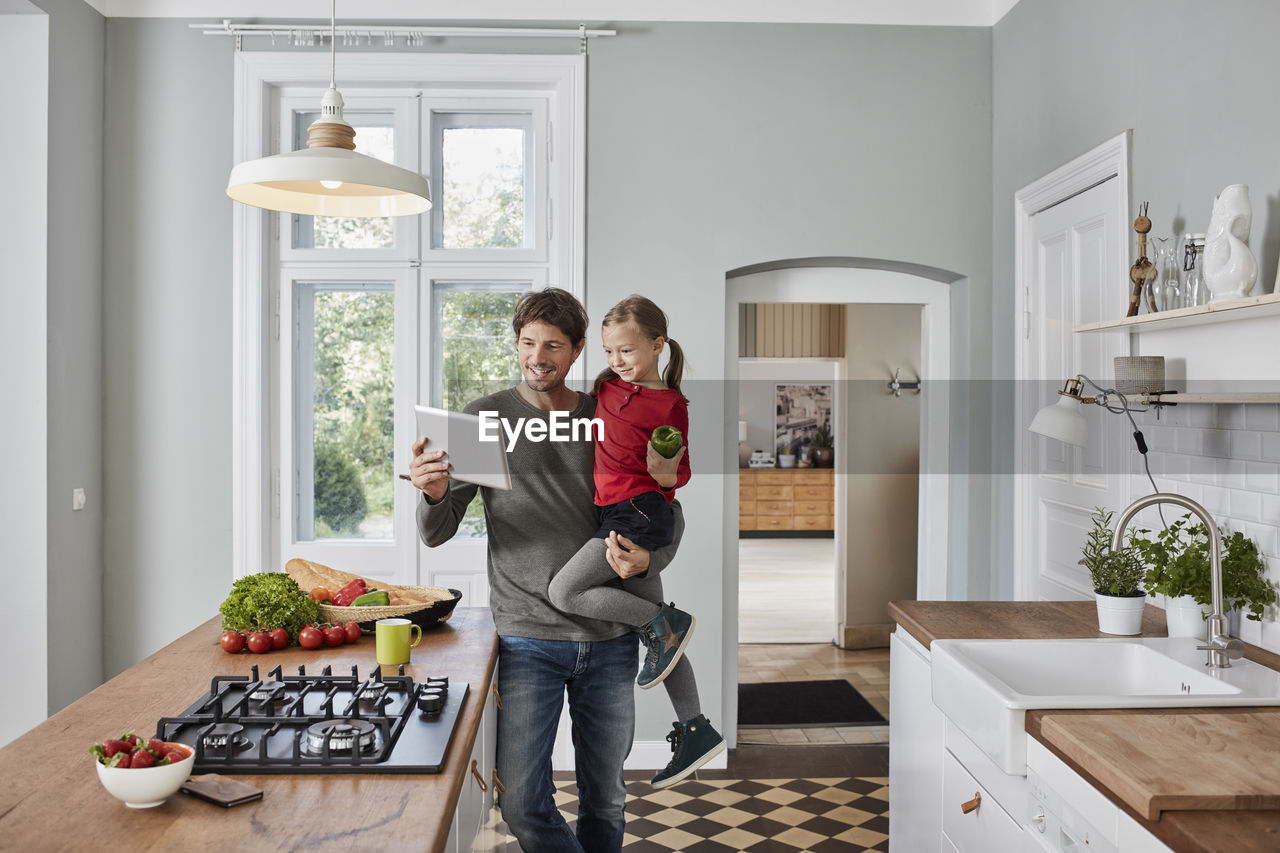 Happy father and daughter with bell pepper and tablet in kitchen