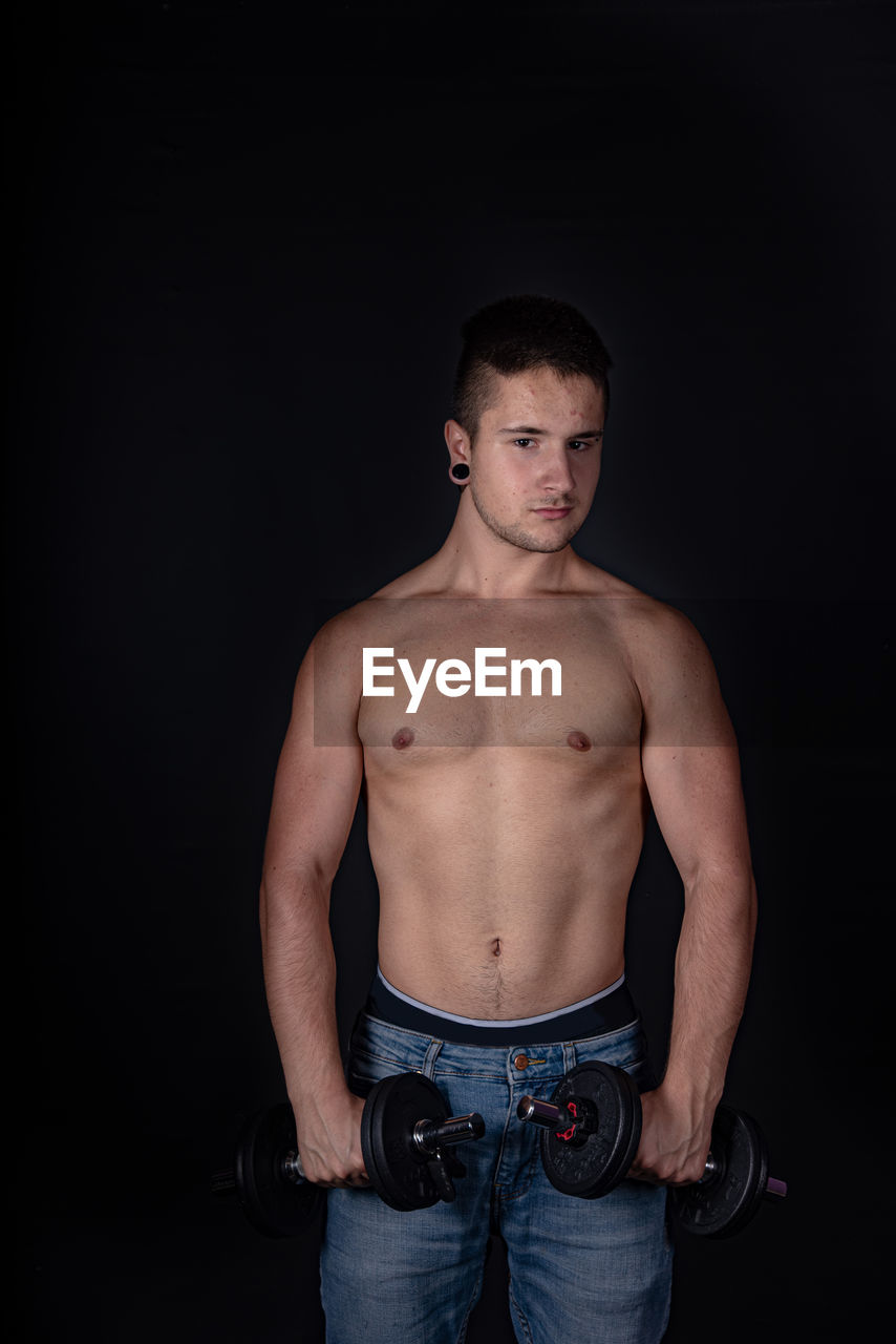 Portrait of shirtless man lifting dumbbells against black background