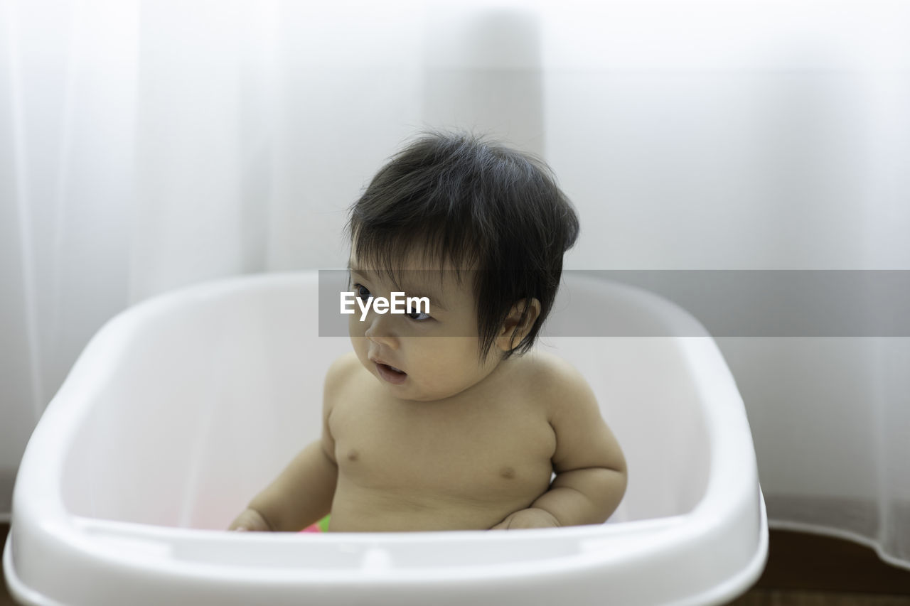 Shirtless baby girl sitting in bathtub