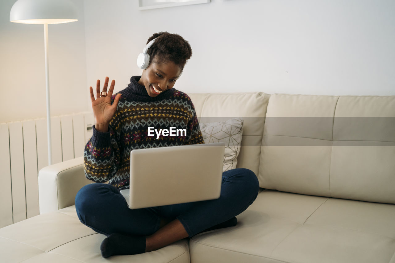 Smiling freelancer waving on video call through laptop in living room