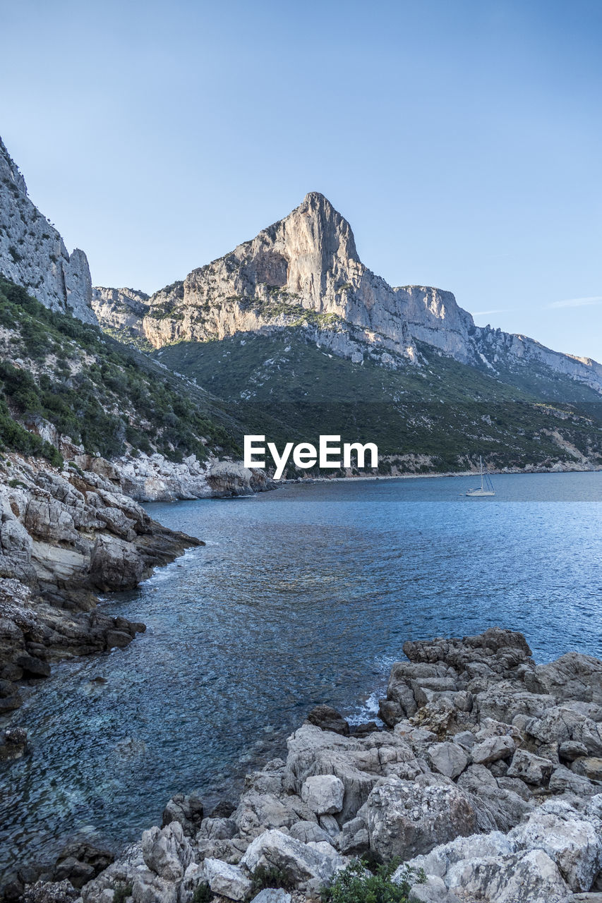 Scenic view of sea and mountains against clear blue sky