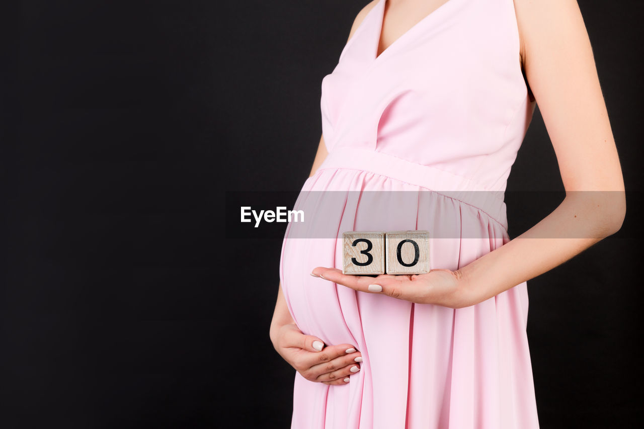 MIDSECTION OF WOMAN STANDING AGAINST PINK GRAY BACKGROUND