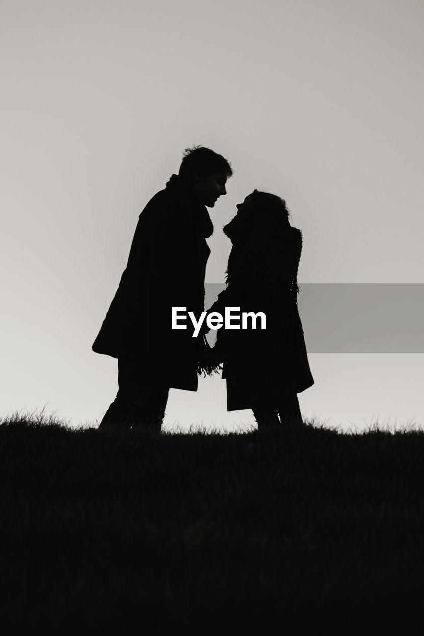 Low angle view of silhouette couple holding hands standing on field against clear sky