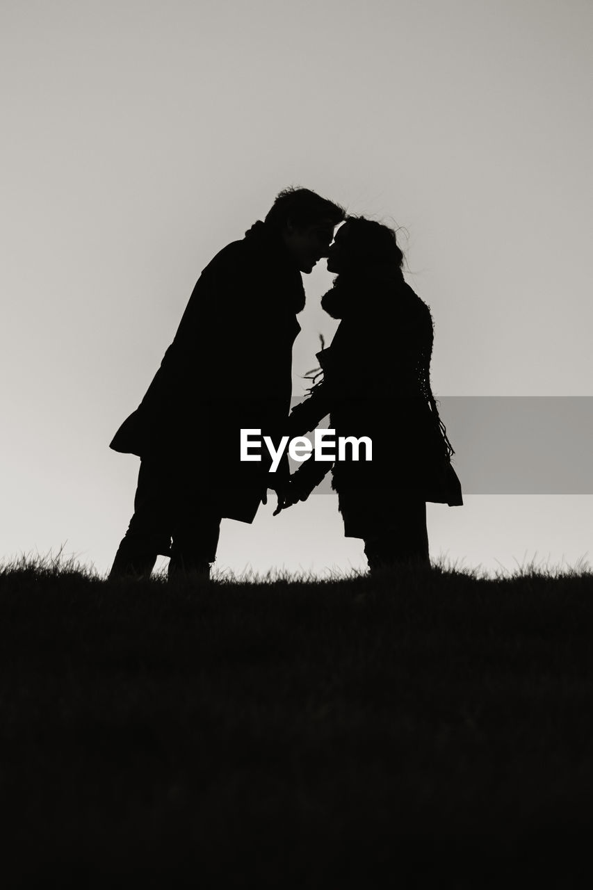 Low angle view of silhouette couple kissing standing on field against clear sky