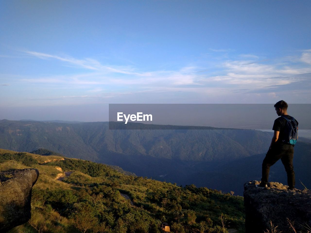 REAR VIEW OF MAN STANDING ON MOUNTAIN AGAINST SKY