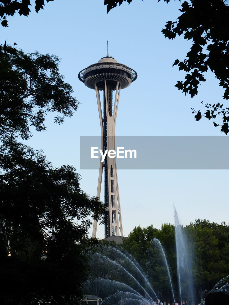 Low angle view of space needle and trees against sky