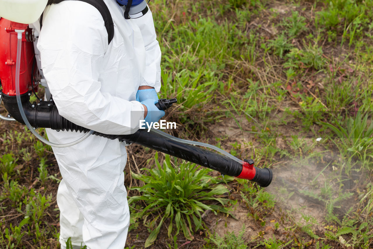 Midsection of person spraying fertilizer on crops in farm