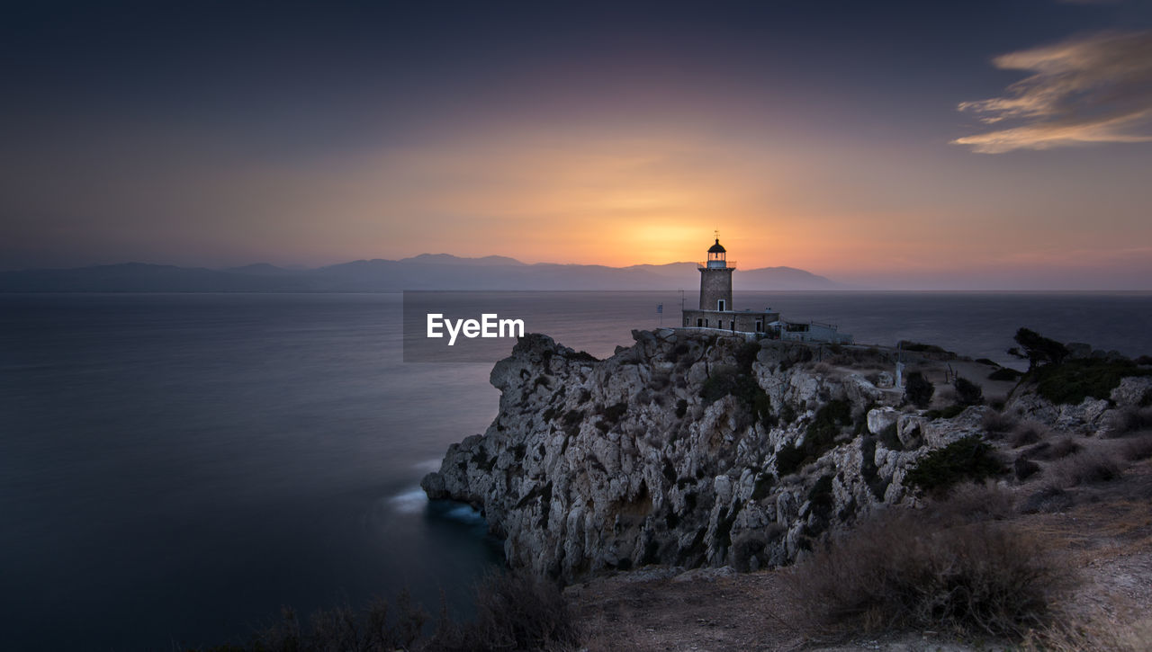 Lighthouse by sea against sky during sunset